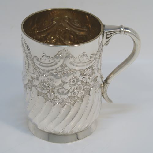 A very pretty Antique Victorian Sterling Silver christening mug, having a round straight-sided body with tucked under belly, all hand-chased with floral, scroll-work, and fluted decoration, a central vacant cartouche, a plain scroll handle, a gold-gilt interior, and all sitting on a collet foot. This beautiful silver mug was made by George Maudsley Jackson of London in 1893. The dimensions of this fine hand-made antique silver christening mug 6.5re height 9.5 cms (3.75 inches), diameter at lip 7 cms (2.6 inches), and it weighs approx. 146g (4.7 troy ounces).   