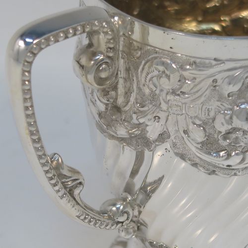 A very pretty Antique Victorian Sterling Silver christening mug, having a round tapering sides, all hand-chased with floral, scroll-work, and fluted decoration, a cast and bead-edged scroll handle, a central vacant cartouche opposite the handle, a gold-gilt interior, and all sitting on a pedestal foot. This beautiful silver christening mug was made by Wakely and Wheeler of London in 1901. The dimensions of this fine hand-made antique silver christening mug are height 9.5 cms (3.75 inches), diameter at lip 7.5 cms (3 inches), and it weighs approx. 161g (5.2 troy ounces).  