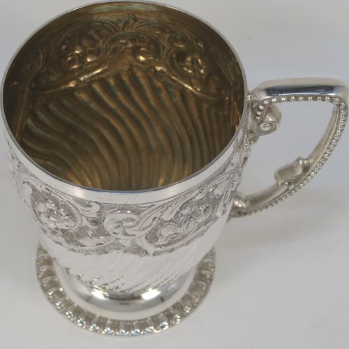 A very pretty Antique Victorian Sterling Silver christening mug, having a round tapering sides, all hand-chased with floral, scroll-work, and fluted decoration, a cast and bead-edged scroll handle, a central vacant cartouche opposite the handle, a gold-gilt interior, and all sitting on a pedestal foot. This beautiful silver christening mug was made by Wakely and Wheeler of London in 1901. The dimensions of this fine hand-made antique silver christening mug are height 9.5 cms (3.75 inches), diameter at lip 7.5 cms (3 inches), and it weighs approx. 161g (5.2 troy ounces).  