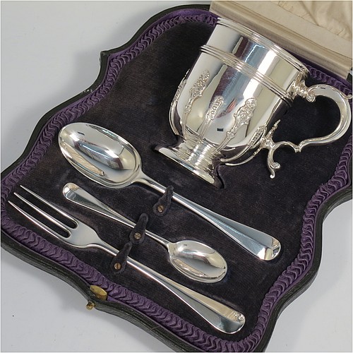 A Sterling Silver christening set consisting of a christening mug with applied strap-work decoration and a scroll handle, and a matching fork and two spoons in the Rattail Hanoverian pattern, all in a cream satin and blue velvet-lined presentation box. The christening mug made in London 1919 and the cutlery from 1895 to 1928. The dimensions of this fine hand-made antique silver christening set are height of mug 9 cms (3.7 inches), length of fork 16 cms (6.25 inches), and with a total weight of approx. 280g (9 troy ounces).