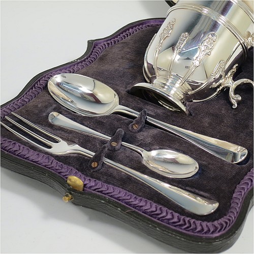 A Sterling Silver christening set consisting of a christening mug with applied strap-work decoration and a scroll handle, and a matching fork and two spoons in the Rattail Hanoverian pattern, all in a cream satin and blue velvet-lined presentation box. The christening mug made in London 1919 and the cutlery from 1895 to 1928. The dimensions of this fine hand-made antique silver christening set are height of mug 9 cms (3.7 inches), length of fork 16 cms (6.25 inches), and with a total weight of approx. 280g (9 troy ounces).