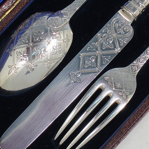 An Antique Victorian Sterling Silver christening set, having a knife, fork, and spoon, all hand-engraved with geometrical and floral work, and all sitting in their original dark blue satin and velvet-lined presentation box. Made by George Adams of London in 1871. The dimensions of this fine hand-made antique silver christening set are length of knife 19 cms (7.5 inches), with a total weight of approx. 100g (3 troy ounces).