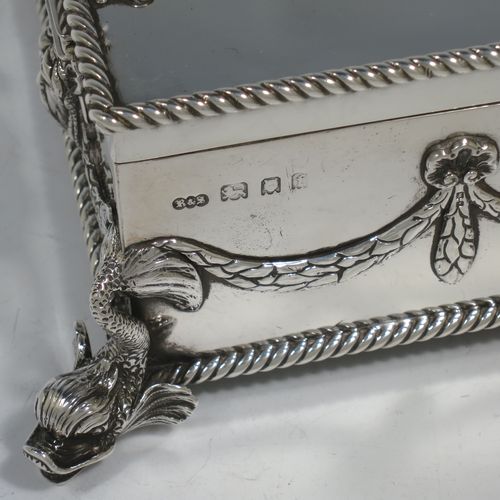 A very handsome and unusual Neptune themed Antique Victorian Sterling Silver cigar / cigarette box, having a rectangular body with applied rope-twist borders, laurel-leaf swags, Neptune face masks, and inter-twined dolphins, a hinged lid with an applied central oval cartouche with a scene of Neptune, mermaids, and sea-horses, a varnished wood-lined interior, and all sitting on four cast dolphin feet. Made by Reid and Sons of London in 1901. The dimensions of this fine hand-made antique silver table box are length 26 cms (10 inches), width 14 cms (5.5 inches), and height 8 cms (3 inches).