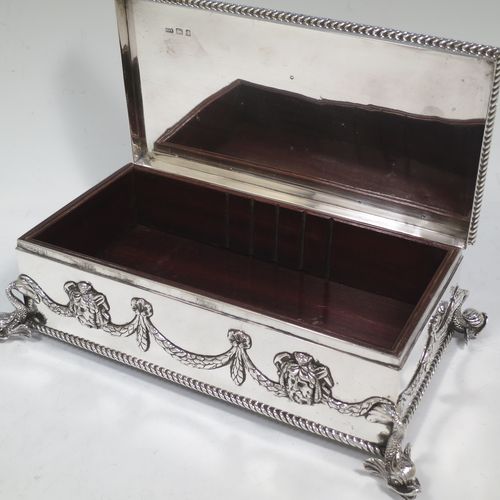 A very handsome and unusual Neptune themed Antique Victorian Sterling Silver cigar / cigarette box, having a rectangular body with applied rope-twist borders, laurel-leaf swags, Neptune face masks, and inter-twined dolphins, a hinged lid with an applied central oval cartouche with a scene of Neptune, mermaids, and sea-horses, a varnished wood-lined interior, and all sitting on four cast dolphin feet. Made by Reid and Sons of London in 1901. The dimensions of this fine hand-made antique silver table box are length 26 cms (10 inches), width 14 cms (5.5 inches), and height 8 cms (3 inches).