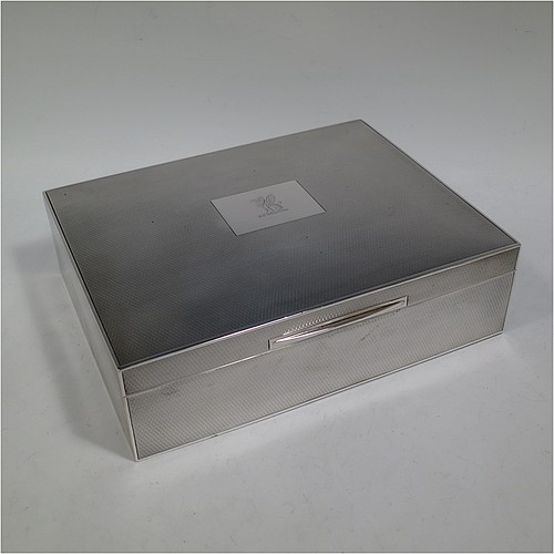 A large and handsome Sterling Silver cigarette or cigar humidor table box, having a rectangular straight-sided body with all over engine-turned decoration, a hinged lid having an applied thumb-piece and central cartouche, a gold-gilt and cedar wood-lined interior, with two removable dividers. Made by Goldsmiths and Silversmiths of London in 1937. The dimensions of this fine hand-made silver table box are length 23 cms (9 inches), width 18 cms (7 inches), and height 7 cms (2.75 inches). Please note that this item is crested on the cartouche.   