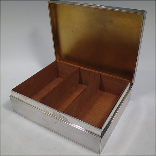 A large and handsome Sterling Silver cigarette or cigar humidor table box, having a rectangular straight-sided body with all over engine-turned decoration, a hinged lid having an applied thumb-piece and central cartouche, a gold-gilt and cedar wood-lined interior, with two removable dividers. Made by Goldsmiths and Silversmiths of London in 1937. The dimensions of this fine hand-made silver table box are length 23 cms (9 inches), width 18 cms (7 inches), and height 7 cms (2.75 inches). Please note that this item is crested on the cartouche.