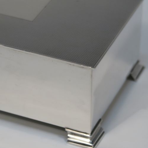 A very elegant Sterling Silver Art Deco style cigarette / cigar table box, having a very plain rectangular body with straight sides, a hinged lid with engine-turned decoration, a central vacant cartouche and thumb-piece, a wooden cedar-lined interior with two dividers, and all sitting on four stepped corner feet. This handsome silver table box was made by Mappin & Webb of London in 1947. The dimensions of this fine hand-made Art Deco silver table box are length 18 cms (7 inches), height 6 cms (2.5 inches), and width 9.5 cms (3.75 inches).