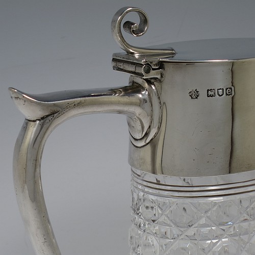 A very handsome Antique Victorian Sterling Silver and hand-cut crystal claret jug, having a plain oval mount, a hinged flat lid with scroll finial, a plain scroll handle with thumb-piece, together with a hand-cut Hobnail pattern oval body with straight tapering sides, and with a star-cut flat base. Made by William Hutton and Sons of London in 1900. The dimensions of this fine hand-made antique silver and crystal claret jug are height 27 cms (10.75 inches), and length 16.5 cms (6.5 inches).