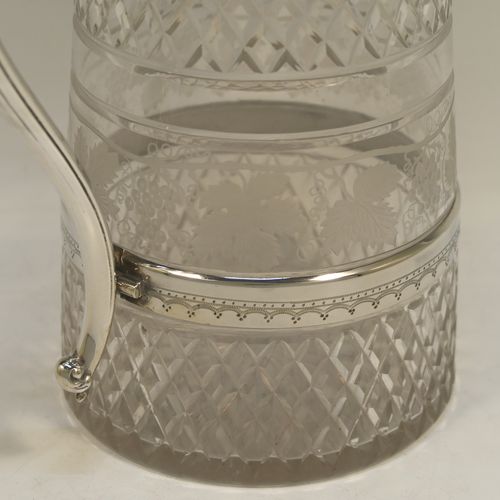A very handsome and large Antique Victorian Silver Plated and hand-cut crystal claret jug, having a hand-engraved mount with floral decoration, a Bacchus face on the spout, a hinged stepped and domed lid with cast finial, a scroll side handle attached to a lower strengthening girdle, and a round hand-cut straight-sided body with a single band of hand-engraved frosted cut work in a grapevine pattern with two bands of hobnail pattern above and below, all sitting on a flat base with a star-cut. Made in ca.1880. The dimensions of this fine hand-made antique silver-plated and crystal claret jug are height 29 cms (11.5 inches), length 20 cms (8 inches), and diameter at the base is 13 cms (5 inches).