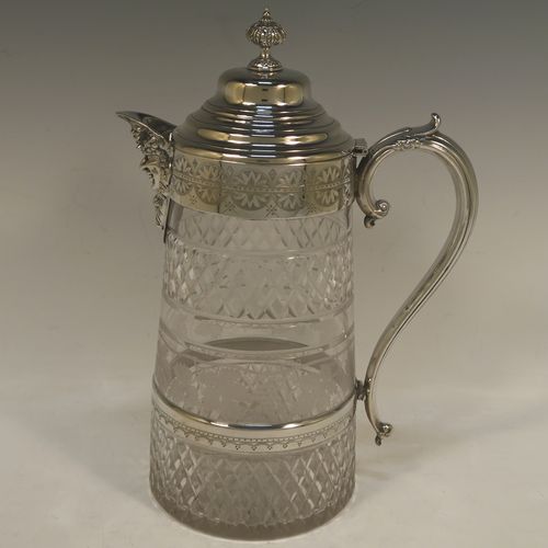 A very handsome and large Antique Victorian Silver Plated and hand-cut crystal claret jug, having a hand-engraved mount with floral decoration, a Bacchus face on the spout, a hinged stepped and domed lid with cast finial, a scroll side handle attached to a lower strengthening girdle, and a round hand-cut straight-sided body with a single band of hand-engraved frosted cut work in a grapevine pattern with two bands of hobnail pattern above and below, all sitting on a flat base with a star-cut. Made in ca.1880. The dimensions of this fine hand-made antique silver-plated and crystal claret jug are height 29 cms (11.5 inches), length 20 cms (8 inches), and diameter at the base is 13 cms (5 inches).
