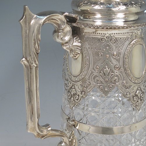 An Antique Victorian Sterling Silver and hand-cut crystal claret jug, having a hand-chased mount with floral decoration, oval vacant cartouches either side, a Bacchus face spout, a hinged lid with floral chasing and a cast finial, a cast scroll handle attached to a retaining ring, together with a hand-cut crystal body with hobnail-cut pattern. Made by Charles Boyton of London in 1882. The dimensions of this fine hand-made antique silver and crystal claret jug are height 29 cms (11.5 inches), and length 19 cms (7.5 inches).