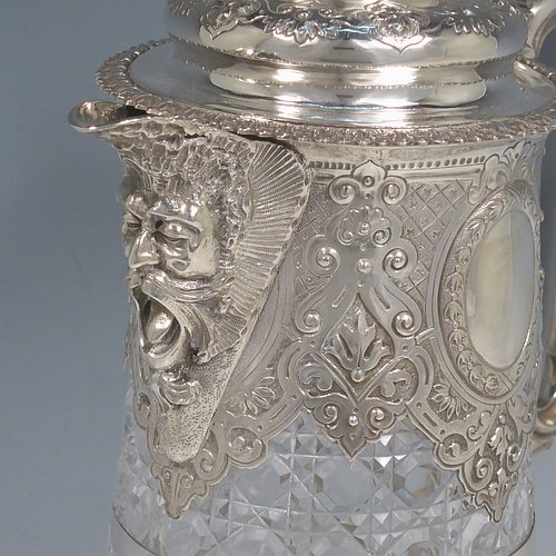 An Antique Victorian Sterling Silver and hand-cut crystal claret jug, having a hand-chased mount with floral decoration, oval vacant cartouches either side, a Bacchus face spout, a hinged lid with floral chasing and a cast finial, a cast scroll handle attached to a retaining ring, together with a hand-cut crystal body with hobnail-cut pattern. Made by Charles Boyton of London in 1882. The dimensions of this fine hand-made antique silver and crystal claret jug are height 29 cms (11.5 inches), and length 19 cms (7.5 inches).