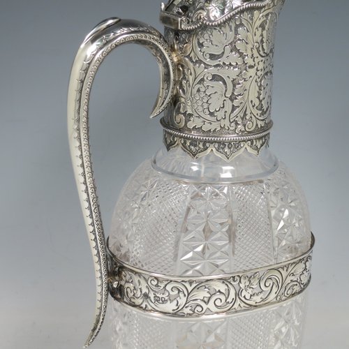 An Antique Victorian Sterling Silver and hand-cut crystal claret jug, having a hand-chased mount with floral decoration and a wavey bead-edged border, a hinged lid with cast floral finial, a hand-chased and engraved scroll handle attached to a hand-pierced floral band, together with an oval cross-section hand-cut Webb crystal body with star-cut panels, all sitting on a matching collet foot. Made by Gibson & Langland of London in 1890. The dimensions of this fine hand-made antique silver and crystal claret jug are height 31 cms (12.25 inches), and length 15 cms (6 inches).