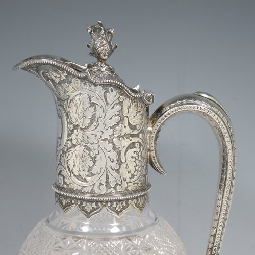 An Antique Victorian Sterling Silver and hand-cut crystal claret jug, having a hand-chased mount with floral decoration and a wavey bead-edged border, a hinged lid with cast floral finial, a hand-chased and engraved scroll handle attached to a hand-pierced floral band, together with an oval cross-section hand-cut Webb crystal body with star-cut panels, all sitting on a matching collet foot. Made by Gibson & Langland of London in 1890. The dimensions of this fine hand-made antique silver and crystal claret jug are height 31 cms (12.25 inches), and length 15 cms (6 inches).