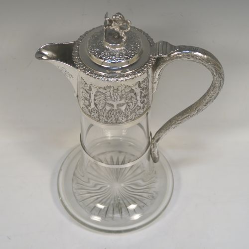 A very handsome Antique Victorian Sterling Silver and hand-cut crystal claret jug, having an ornate Bacchus style round mount with hand-chased grapevine work, a tendril style sided handle with a security ring, a hinged lid with a cast rampant lion and shield finial, together with a hand-cut crystal round body with straight sides and a tucked under belly above a flat star-cut base. This beautiful antique silver claret jug was made by Charles Boyton of London in 1889. The dimensions of this fine hand-made antique silver and crystal claret jug are height 27 cms (10.5 inches), and length 18.5 cms (7.5 inches).
