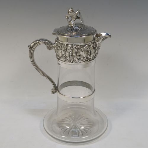 A very handsome Antique Victorian Silver Plated and hand-cut crystal claret jug, having an ornate  Bacchus style round mount with hand-chased figural work, a cast side handle with a plain round security ring, a hinged lid with a cast rampant lion and shield finial, together with a hand-cut crystal round body with straight sides and a tucked under belly above a flat star-cut base. Made by Hukin and Heath  of Sheffield in ca. 1880. The dimensions of this fine hand-made antique silver-plated and crystal claret jug are height 26 cms (10.25 inches), and length 16 cms (6.3 inches).  