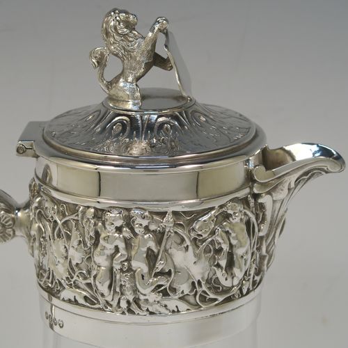 A very handsome Antique Victorian Silver Plated and hand-cut crystal claret jug, having an ornate Bacchus style round mount with hand-chased figural work, a cast side handle with a plain round security ring, a hinged lid with a cast rampant lion and shield finial, together with a hand-cut crystal round body with straight sides and a tucked under belly above a flat star-cut base. Made by Hukin and Heath of Sheffield in ca. 1880. The dimensions of this fine hand-made antique silver-plated and crystal claret jug are height 26 cms (10.25 inches), and length 16 cms (6.3 inches).