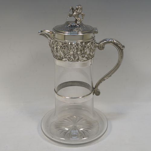 A very handsome Antique Victorian Silver Plated and hand-cut crystal claret jug, having an ornate Bacchus style round mount with hand-chased figural work, a cast side handle with a plain round security ring, a hinged lid with a cast rampant lion and shield finial, together with a hand-cut crystal round body with straight sides and a tucked under belly above a flat star-cut base. Made by Hukin and Heath of Sheffield in ca. 1880. The dimensions of this fine hand-made antique silver-plated and crystal claret jug are height 26 cms (10.25 inches), and length 16 cms (6.3 inches).