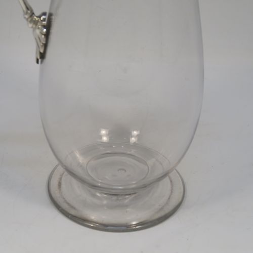 A very elegant Antique Victorian Sterling Silver and hand-cut crystal claret jug, having a plain round mount with applied bead-edged borders, a plain square cross-section side handle, a hinged stepped lid with a cast round finial, together with a hand-cut crystal round body with straight tapering sides and a tucked under belly above a pedestal foot. This handsome silver and crystal claret jug was made by Charles Favell of Sheffield in 1875. The dimensions of this fine hand-made antique silver and crystal claret jug are height 28 cms (11 inches), and length 13.5 cms (5.25 inches). Please note that this item has two oval cartouches with bead borders one of which is engraved with a part crest.