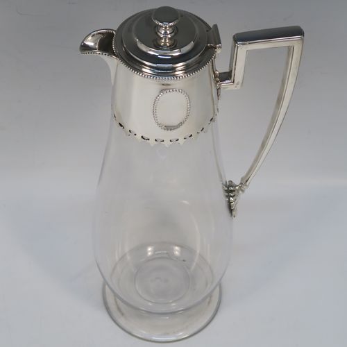 A very elegant Antique Victorian Sterling Silver and hand-cut crystal claret jug, having a plain round mount with applied bead-edged borders, a plain square cross-section side handle, a hinged stepped lid with a cast round finial, together with a hand-cut crystal round body with straight tapering sides and a tucked under belly above a pedestal foot. This handsome silver and crystal claret jug was made by Charles Favell of Sheffield in 1875. The dimensions of this fine hand-made antique silver and crystal claret jug are height 28 cms (11 inches), and length 13.5 cms (5.25 inches). Please note that this item has two oval cartouches with bead borders one of which is engraved with a part crest.