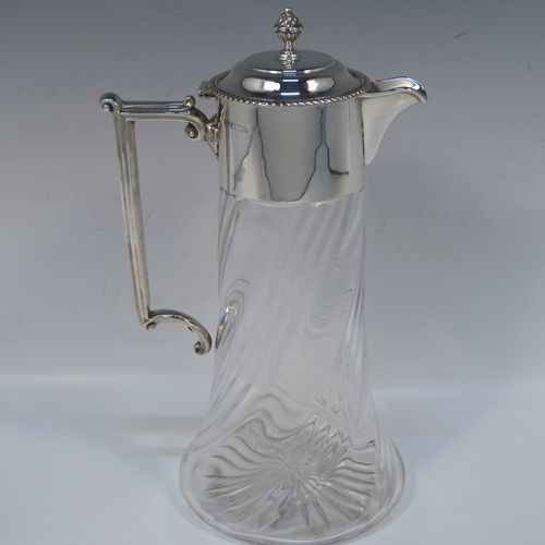 A very handsome Antique late Victorian Sterling Silver and hand-cut crystal claret jug, having a plain round mount, a hinged domed lid with a gadroon border and finial, an angular and scrolled side-handle, and a round hand-cut straight-sided body with flared base, having swirl-fluted decoration and a star-cut base. This elegant silver and crystal claret jug was made by William Hutton of Sheffield in 1901. The dimensions of this fine hand-made antique silver and crystal claret jug are height 26 cms (10.25 inches), and length 15 cms (6 inches).  