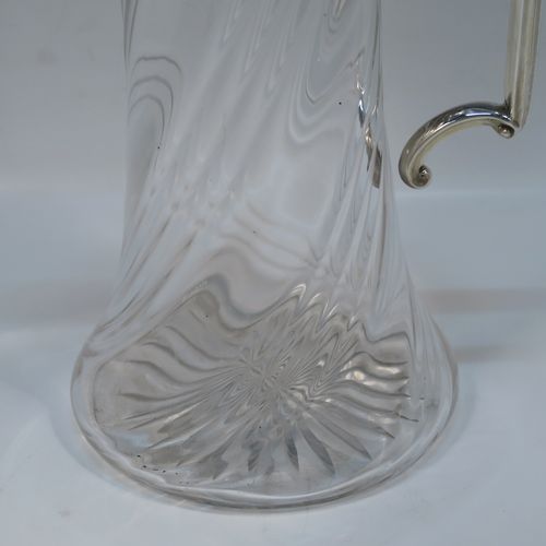 A very handsome Antique late Victorian Sterling Silver and hand-cut crystal claret jug, having a plain round mount, a hinged domed lid with a gadroon border and finial, an angular and scrolled side-handle, and a round hand-cut straight-sided body with flared base, having swirl-fluted decoration and a star-cut base. This elegant silver and crystal claret jug was made by William Hutton of Sheffield in 1901. The dimensions of this fine hand-made antique silver and crystal claret jug are height 26 cms (10.25 inches), and length 15 cms (6 inches).