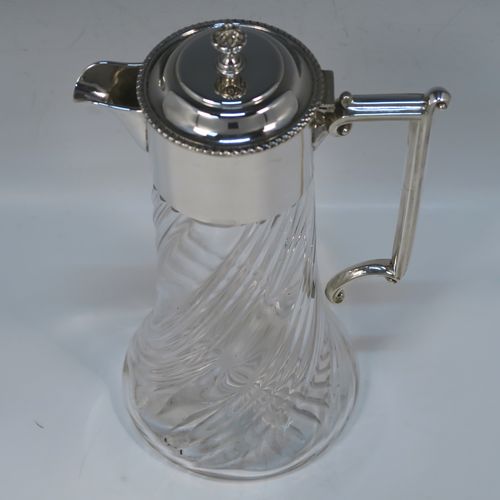 A very handsome Antique late Victorian Sterling Silver and hand-cut crystal claret jug, having a plain round mount, a hinged domed lid with a gadroon border and finial, an angular and scrolled side-handle, and a round hand-cut straight-sided body with flared base, having swirl-fluted decoration and a star-cut base. This elegant silver and crystal claret jug was made by William Hutton of Sheffield in 1901. The dimensions of this fine hand-made antique silver and crystal claret jug are height 26 cms (10.25 inches), and length 15 cms (6 inches).