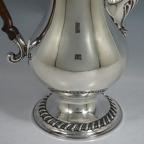 An Antique Georgian Sterling Silver coffee pot, having a plain round bellied body, with applied gadroon borders, a wooden scroll handle, a flame knop finial, and anthemion leaf decorated spout. Made in London in 1774. The dimensions of this fine hand-made antique silver coffee pot are height 30.5 cms (12 inches), length 22 cms (8.75 inches), and it weighs approx. 850g (27.4 troy ounces).    