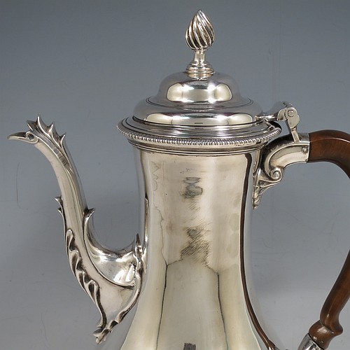 An Antique Georgian Sterling Silver coffee pot, having a plain round bellied body, with applied gadroon borders, a wooden scroll handle, a flame knop finial, and anthemion leaf decorated spout. Made in London in 1774. The dimensions of this fine hand-made antique silver coffee pot are height 30.5 cms (12 inches), length 22 cms (8.75 inches), and it weighs approx. 850g (27.4 troy ounces).    