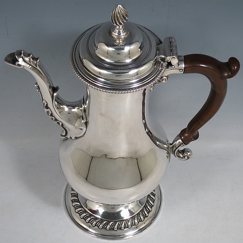An Antique Georgian Sterling Silver coffee pot, having a plain round bellied body, with applied gadroon borders, a wooden scroll handle, a flame knop finial, and anthemion leaf decorated spout. Made in London in 1774. The dimensions of this fine hand-made antique silver coffee pot are height 30.5 cms (12 inches), length 22 cms (8.75 inches), and it weighs approx. 850g (27.4 troy ounces).    