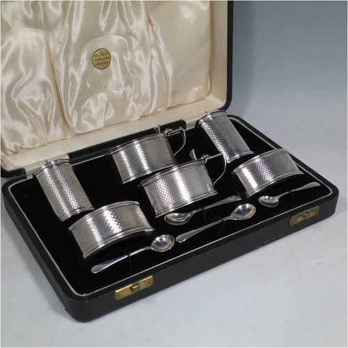 A Sterling Silver Art Deco condiment service, having oval straight-sided bodies with engine-turned decoration, with original blue-glass liners, pull-off lids on the peppers, hinged lids on the mustards, and all in original velvet and satin-lined presentation box. Consisting of two mustard pots, two pepper pots, two salt cellars, and four condiment spoons. Made in Chester and Birmingham from 1930 to 1934. Height of peppers 6.5 cms (2.5 inches), length of mustard 8 cms (3 inches), and a total weight of approx. 248g (8 troy ounces).   