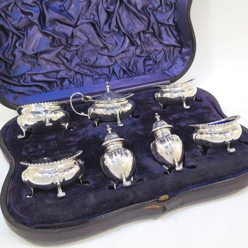 A handsome and large Antique Edwardian Sterling Silver seven-piece condiment service, consisting of a mustard pot with hinged lid and blue-glass liner, four salt cellars with blue-glass liners, and two pepper pots with pull-off lids, all with scroll fluted bellied bodies and sitting four scroll feet, and all fitted into their original dark blue satin and velvet-lined red presentation box. Made by James Round of London  in 1903. The dimensions of this fine hand-made condiment service are height of pepper pot 9 cms (3.5 inches), length of mustard pot 9 cms (3.5 inches), and with a total weight of approx. 353g (11.4 troy ounces).   