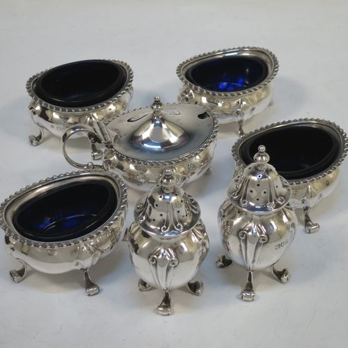 A handsome and large Antique Edwardian Sterling Silver seven-piece condiment service, consisting of a mustard pot with hinged lid and blue-glass liner, four salt cellars with blue-glass liners, and two pepper pots with pull-off lids, all with scroll fluted bellied bodies and sitting four scroll feet, and all fitted into their original dark blue satin and velvet-lined red presentation box. Made by James Round of London in 1903. The dimensions of this fine hand-made condiment service are height of pepper pot 9 cms (3.5 inches), length of mustard pot 9 cms (3.5 inches), and with a total weight of approx. 353g (11.4 troy ounces).