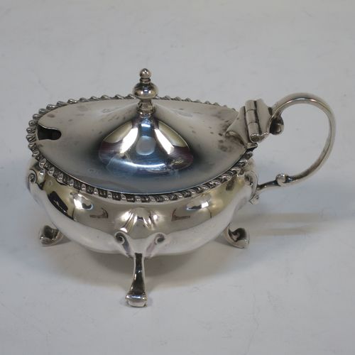 A handsome and large Antique Edwardian Sterling Silver seven-piece condiment service, consisting of a mustard pot with hinged lid and blue-glass liner, four salt cellars with blue-glass liners, and two pepper pots with pull-off lids, all with scroll fluted bellied bodies and sitting four scroll feet, and all fitted into their original dark blue satin and velvet-lined red presentation box. Made by James Round of London in 1903. The dimensions of this fine hand-made condiment service are height of pepper pot 9 cms (3.5 inches), length of mustard pot 9 cms (3.5 inches), and with a total weight of approx. 353g (11.4 troy ounces).