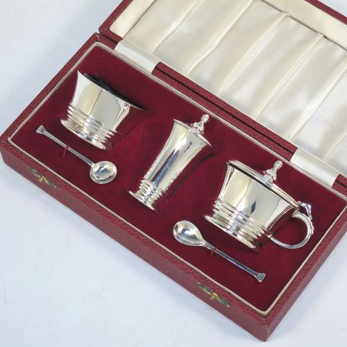 A very elegant Sterling Silver three-piece condiment set in an Art Deco style, consisting of an open salt cellar with a blue glass liner, a pepper pot with pull-off lid, a mustard pot with blue glass liner and hinged lid, together with two original condiment spoons, and all in their cream satin and maroon velvet-lined presentation box. Made by Deakin and Francis of Birmingham in 1970. The dimensions of this fine hand-made silver condiment service are length of mustard pot 7.5 cms (3 inches), height of pepper pot 7 cms (2.75 inches), diameter of salt cellar 6 cms (2.3 inches), and with a total weight of approx. 164g (5.3 troy ounces). 