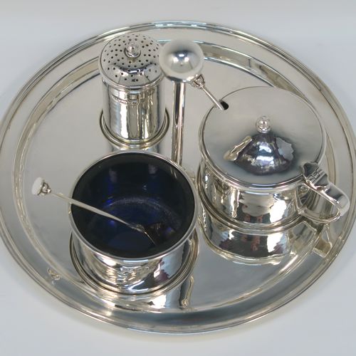 A very elegant and unusual Arts and Crafts style Sterling Silver three-piece condiment, with hand-hammered straight-sided round bodies, consisting of an open salt cellar with a blue glass liner and original spoon, a pepper pot with pull-off lid, a mustard pot with blue glass liner, hinged lid, and original spoon, an all sitting on a circular plate with carrying handle. This handsome silver condiment service was all made by the London Guild of Handicrafts in 1989. The dimensions of this fine hand-made Arts and Crafts style silver condiment set are diameter of holding plate 19 cms (7.5 inches), diameter of mustard and salt pots 6 cms (2.3 inches), height of pepper pot 7 cms (2.75 inches), and with a total weight of approx. 598g (19.3 troy ounces).   