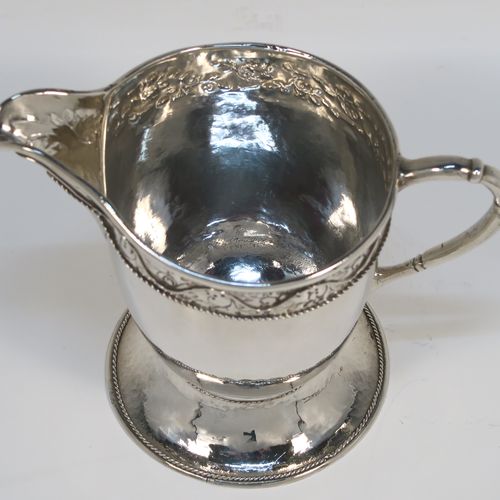 A beautiful Sterling Silver Arts and Crafts style cream or milk jug, having a round body with hand-hammered decoration, with an applied and hand-chased top band of floral work, with a cast rounded side-handle, and all sitting on a spreading round pedestal foot with applied rope-twist borders. This fantastic silver milk or cream jug was made by Harold Edwin Landon of Chester in 1933. The dimensions of this fine hand-made Arts and Crafts jug are height 11.5 cms (4.5 inches), length 14 cms (5.5 inches), and with a weight of approx. 195g (6.3 troy ounces).
