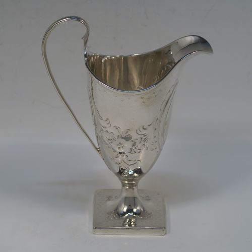 A very pretty Antique Georgian Sterling Silver cream jug, having a round body with tapering sides in a Helmet style, all hand-chased with floral and scroll decoration, a front cartouche with heraldic crest, a scroll handle, and sitting on a pedestal foot with a square base. This beautiful silver cream jug was made by John Denzilow of London in 1788. The dimensions of this fine hand-made antique silver cream jug are length 11.5 cms (4.5 inches), height 15 cms (6 inches), and it weighs approx. 137g (4.4 troy ounces).   