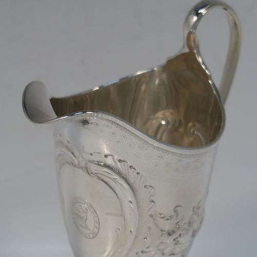 A very pretty Antique Georgian Sterling Silver cream jug, having a round body with tapering sides in a Helmet style, all hand-chased with floral and scroll decoration, a front cartouche with heraldic crest, a scroll handle, and sitting on a pedestal foot with a square base. This beautiful silver cream jug was made by John Denzilow of London in 1788. The dimensions of this fine hand-made antique silver cream jug are length 11.5 cms (4.5 inches), height 15 cms (6 inches), and it weighs approx. 137g (4.4 troy ounces).