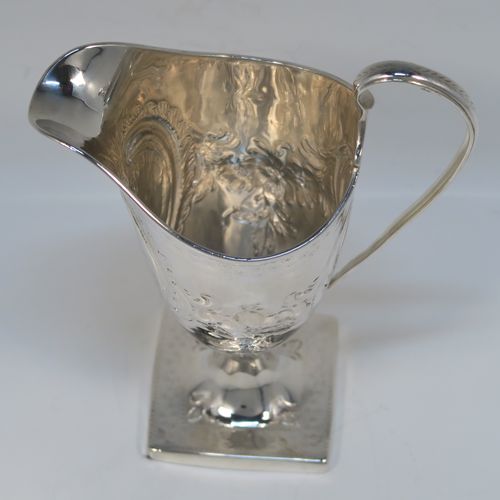 A very pretty Antique Georgian Sterling Silver cream jug, having a round body with tapering sides in a Helmet style, all hand-chased with floral and scroll decoration, a front cartouche with heraldic crest, a scroll handle, and sitting on a pedestal foot with a square base. This beautiful silver cream jug was made by John Denzilow of London in 1788. The dimensions of this fine hand-made antique silver cream jug are length 11.5 cms (4.5 inches), height 15 cms (6 inches), and it weighs approx. 137g (4.4 troy ounces).