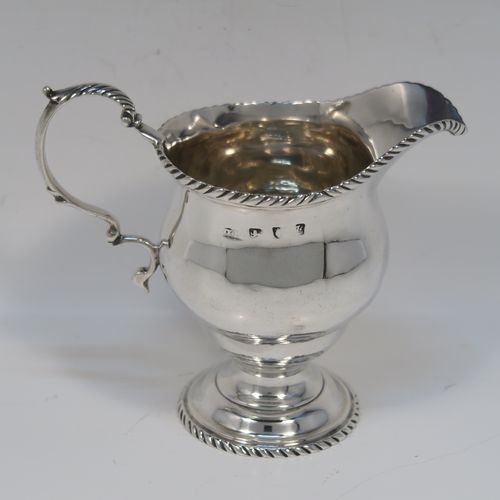 A very elegant Antique Georgian Sterling Silver cream jug, having a round bellied body with applied gadroon borders, a scroll side-handle, and all sitting on a round pedestal foot. This handsome silver cream or milk jug was made Walter Brind of London in 1762. The dimensions of this fine hand-made antique silver milk or cream jug are height 10 cms (4 inches), length 12 cms (4.75 inches), and it weighs approx. 127g (4 troy ounces).   
