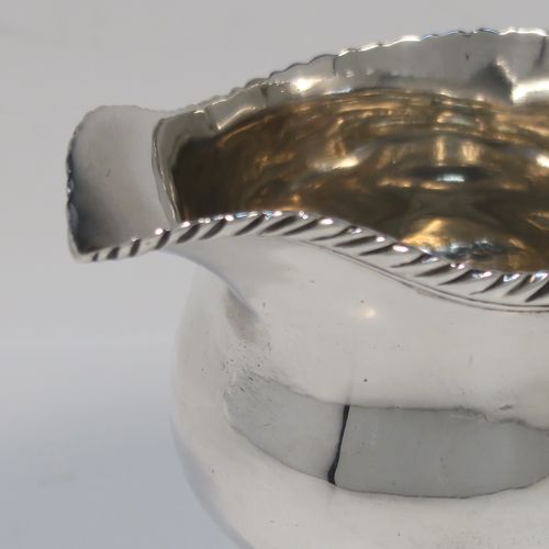 A very elegant Antique Georgian Sterling Silver cream jug, having a round bellied body with applied gadroon borders, a scroll side-handle, and all sitting on a round pedestal foot. This handsome silver cream or milk jug was made Walter Brind of London in 1762. The dimensions of this fine hand-made antique silver milk or cream jug are height 10 cms (4 inches), length 12 cms (4.75 inches), and it weighs approx. 127g (4 troy ounces).