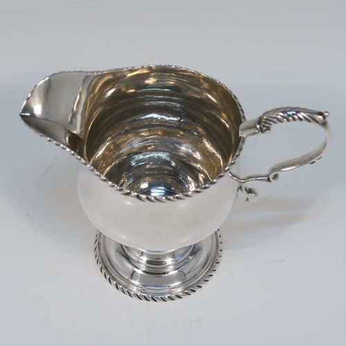 A very elegant Antique Georgian Sterling Silver cream jug, having a round bellied body with applied gadroon borders, a scroll side-handle, and all sitting on a round pedestal foot. This handsome silver cream or milk jug was made Walter Brind of London in 1762. The dimensions of this fine hand-made antique silver milk or cream jug are height 10 cms (4 inches), length 12 cms (4.75 inches), and it weighs approx. 127g (4 troy ounces).
