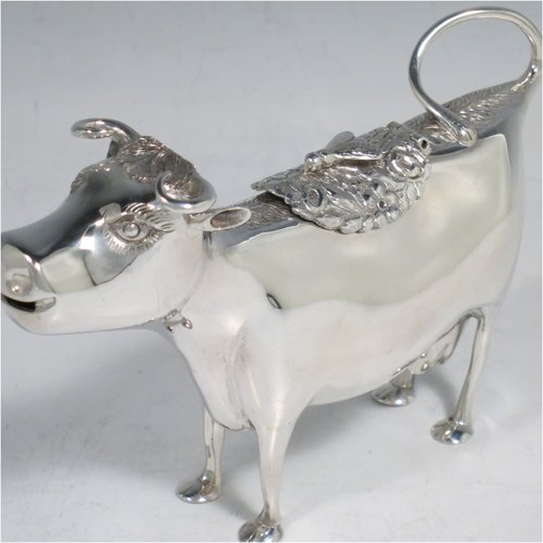 An Antique Victorian Sterling Silver Dutch Cow cream jug, in a George II Cow creamer style, having a hinged lid with hand-chased flowers and an applied model of a bee, with a handle made from from the cows looped tail, and a spout made from the cows mouth, all sitting on four hoof feet. Made in ca. 1880 with Dutch hallmarks. The dimensions of this fine hand-made silver cow creamer are length 14.5 cms (5.75 inches), height 10 cms (4 inches), and it weighs approx. 126g (4 troy ounces).
