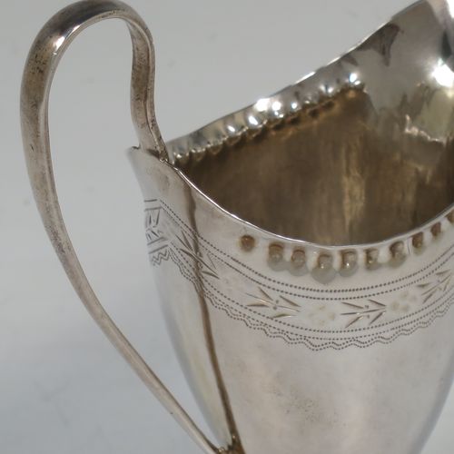 A pretty Antique Georgian Sterling Silver cream jug, having a round body with tapering sides in a Helmet style, with an upper band of floral decoration, a vacant front cartouche, a hand-punched bead border, a scroll handle, and sitting on a pedestal foot with a square base. Made by Peter and Anne Bateman of London in 1792. The dimensions of this fine hand-made antique silver cream jug are length 10 cms (4 inches), height 13 cms (5 inches), and it weighs approx. 84g (2.7 troy ounces).