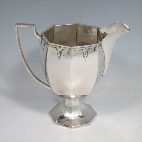 A Sterling Silver Arts & Crafts style large milk jug, having a panelled tapering body with a hand-hammered finish, an applied geometrical border, a plain handle and spout, and all sitting on a pedestal foot. Made by the Guild of Handicrafts of London in 1934. The dimensions of this fine hand-made silver cream or milk jug are height 13.5 cms (5.25 inches), length 15 cms (6 inches), and it weighs approx. 260g (8.4 troy ounces).    