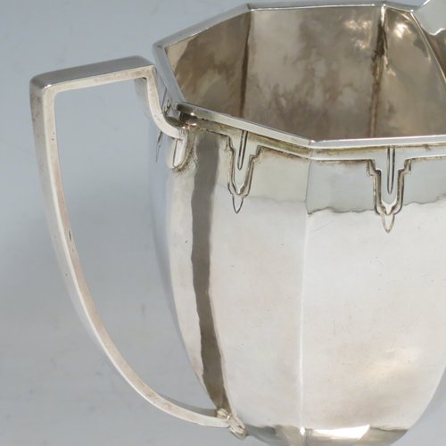 A Sterling Silver Arts & Crafts style large milk jug, having a panelled tapering body with a hand-hammered finish, an applied geometrical border, a plain handle and spout, and all sitting on a pedestal foot. Made by the Guild of Handicrafts of London in 1934. The dimensions of this fine hand-made silver cream or milk jug are height 13.5 cms (5.25 inches), length 15 cms (6 inches), and it weighs approx. 260g (8.4 troy ounces).