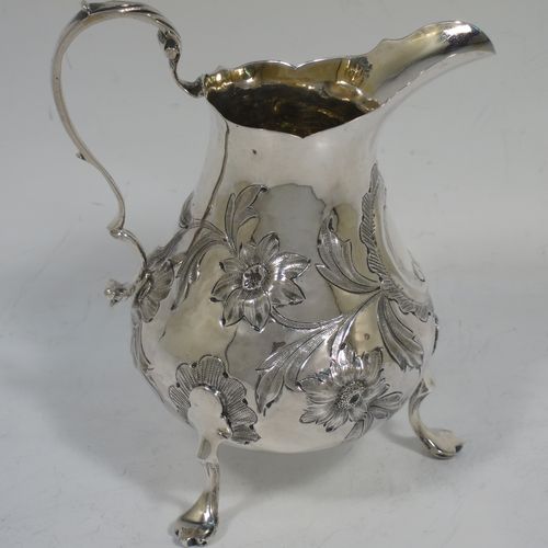 A very pretty Antique early Victorian Sterling Silver cream or milk jug having a round bellied body with hand-chased floral decoration surrounding a vacant cartouche, a scroll handle with anthemion leaf thumb-piece, a shaped border with a spout, a gold-gilt interior, and sitting on three cast trefoil feet. Made by William Hunter of London in 1845. The dimensions of this fine hand-made antique silver cream jug are height 11.5 cms (4.5 inches), length 10 cms (4 inches), and it weighs approx. 115g (3.7 troy ounces).    