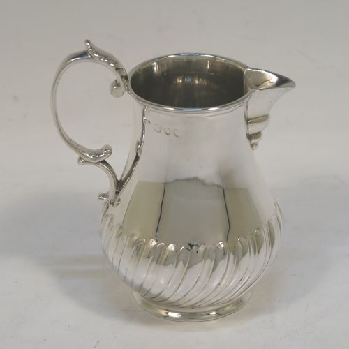 A pretty Antique Victorian Sterling Silver cream jug, in a George I Sparrow-Beak style with a bellied body having hand-chased half-fluted decoration, a plain scroll side-handle, a sparrow-beak spout, and sitting on a collet foot. This beautiful silver cream jug was made by Arthur Sibley of London in 1890. The dimensions of this fine hand-made antique silver cream jug are height 11 cms (4.25 inches), length 9 cms (3.5 inches), and it weighs approx. 121g (3.9 troy ounces).   