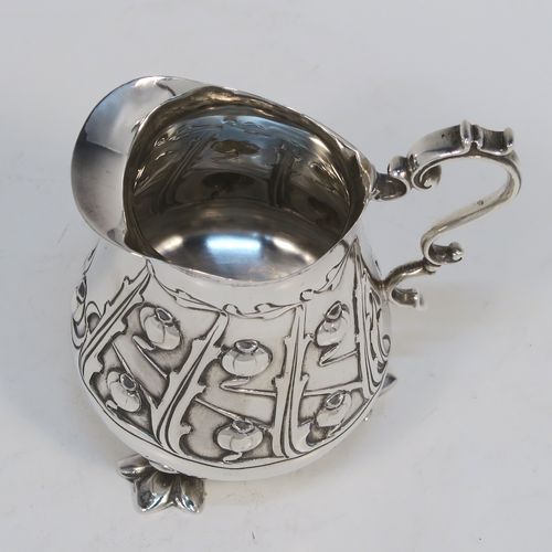 A very pretty Arts and Crafts Antique Edwardian Sterling Silver cream or milk jug having a round bellied body with hand-chased poppy seed head and leaf floral decoration, a cast scroll side-handle, and sitting on three cast trefoil feet. This beautiful Arts and Crafts style silver milk jug was made by Lee and Wigfull (Henry Wigfull) of Sheffield in 1903. The dimensions of this fine hand-made antique silver cream jug are height 9 cms (3.5 inches), length 9 cms (3.5 inches), and it weighs approx. 114g (3.7 troy ounces).